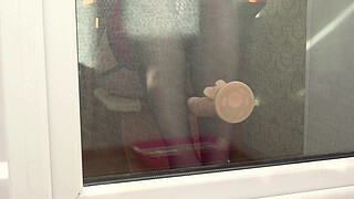A neighbor watches through the window, as a MILF fucks herself with a dildo by the balcony door. Beautiful ass in doggy style.